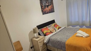 A bedroom with a bed, a nightstand, a chair, a painting, and a window with curtains. - Modern 2-Bed Apt Near Hospital and University of Birmingham (Birmingham)