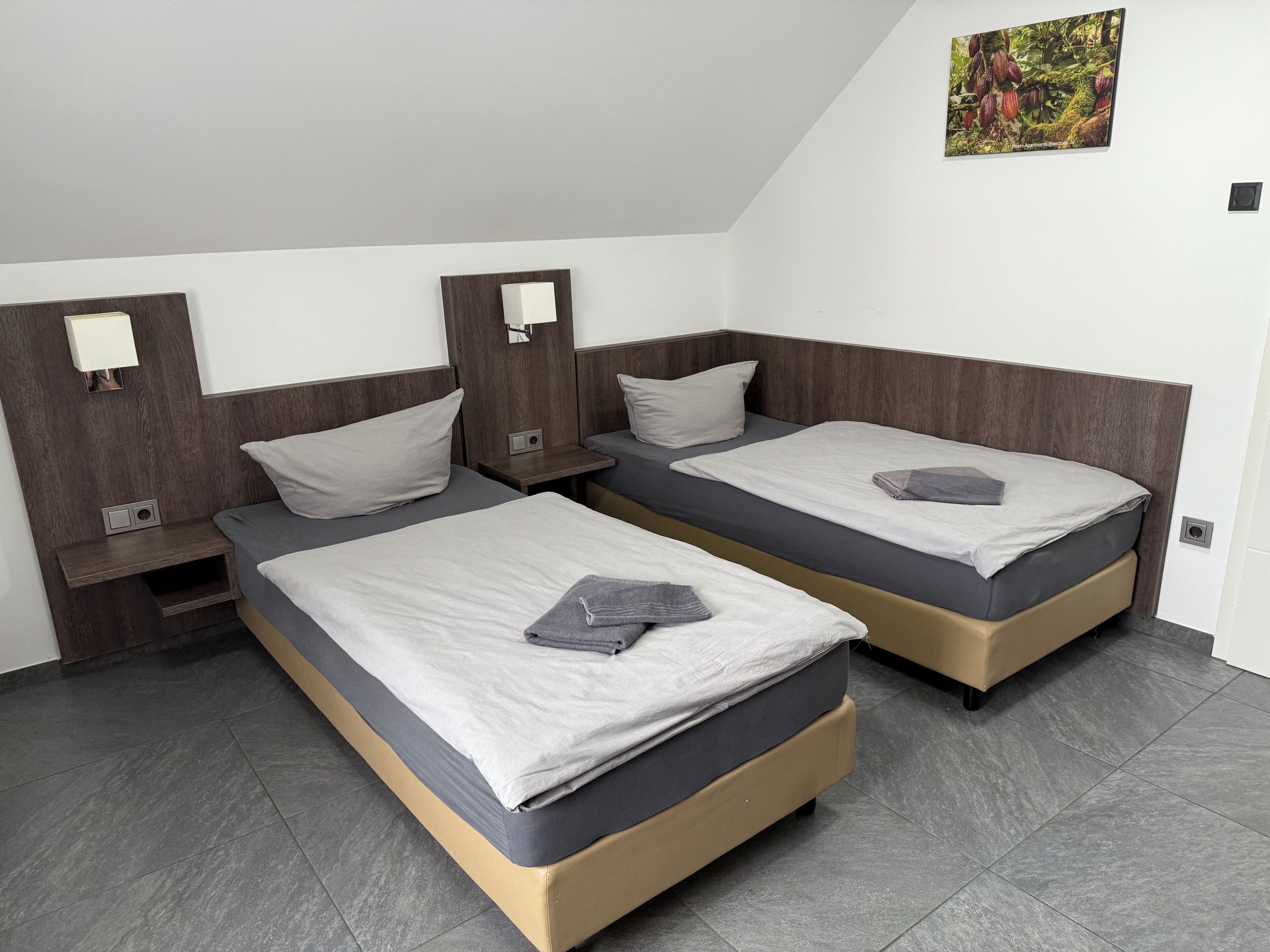 A room with two beds, a nightstand, a wall-mounted TV, and a small picture.