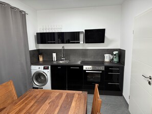 A compact kitchen with a washing machine, a coffee maker, and a microwave. - Blauer Stein - Core it02- Haus (Bergheim)