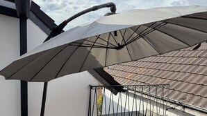Eine Dachterrasse mit einer Pergola und Sonnenschirmen, einem Ziegeldach und einem Metallgeländer.