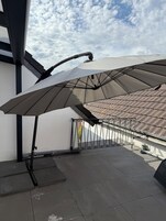 Una terraza en la azotea con pérgola, sombrillas, techo de baldosas y barandilla de metal.