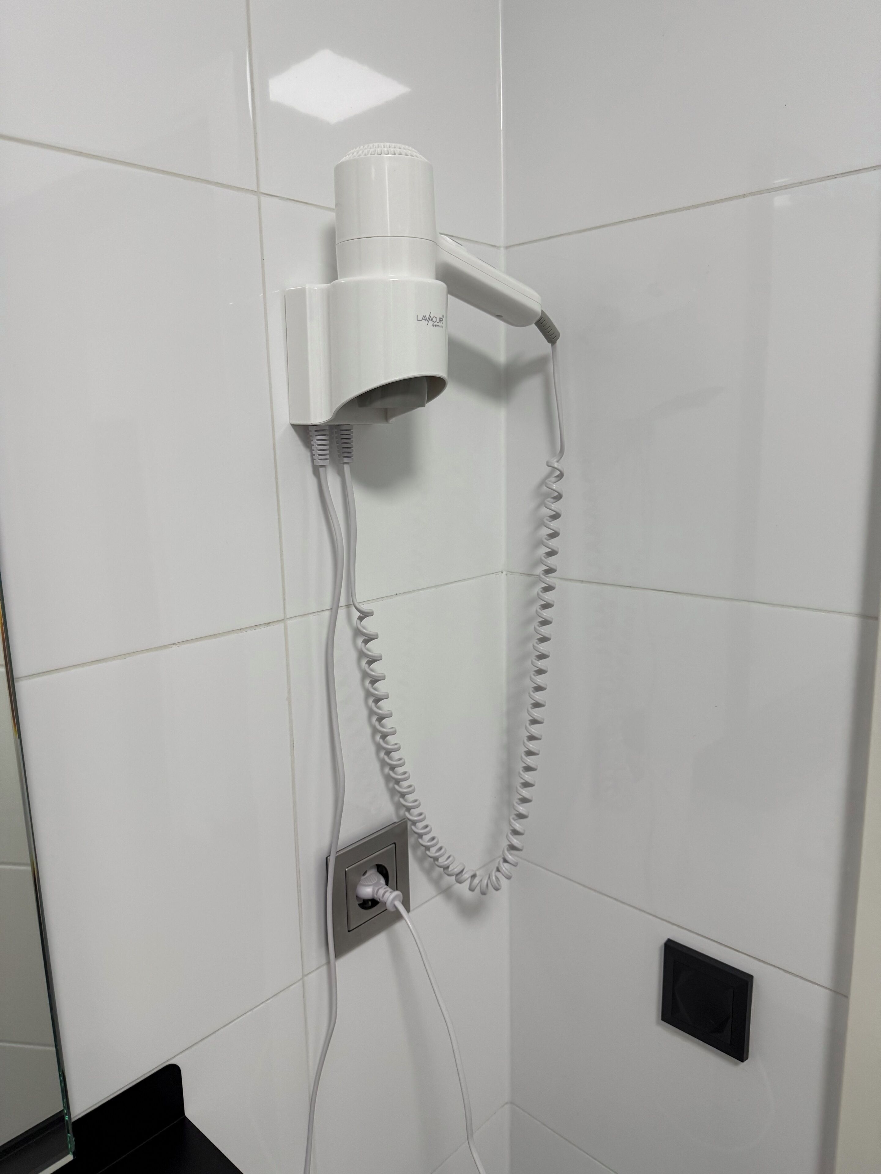 A hairdryer mounted on a wall with a power cord plugged into a wall socket.