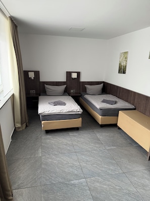 A hotel room with two beds, a bench, a window with curtains, and a wall-mounted picture. - Blauer Stein - Core it02- Haus (Bergheim)