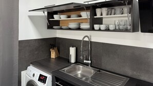Eine moderne Küche mit einer integrierten Waschmaschine, einer Spüle aus Edelstahl und Regalen mit Geschirr und Gläsern.