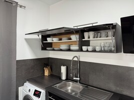 Una cocina moderna con lavadora integrada, un lavaplatos de acero inoxidable y estantes con platos y vasos.