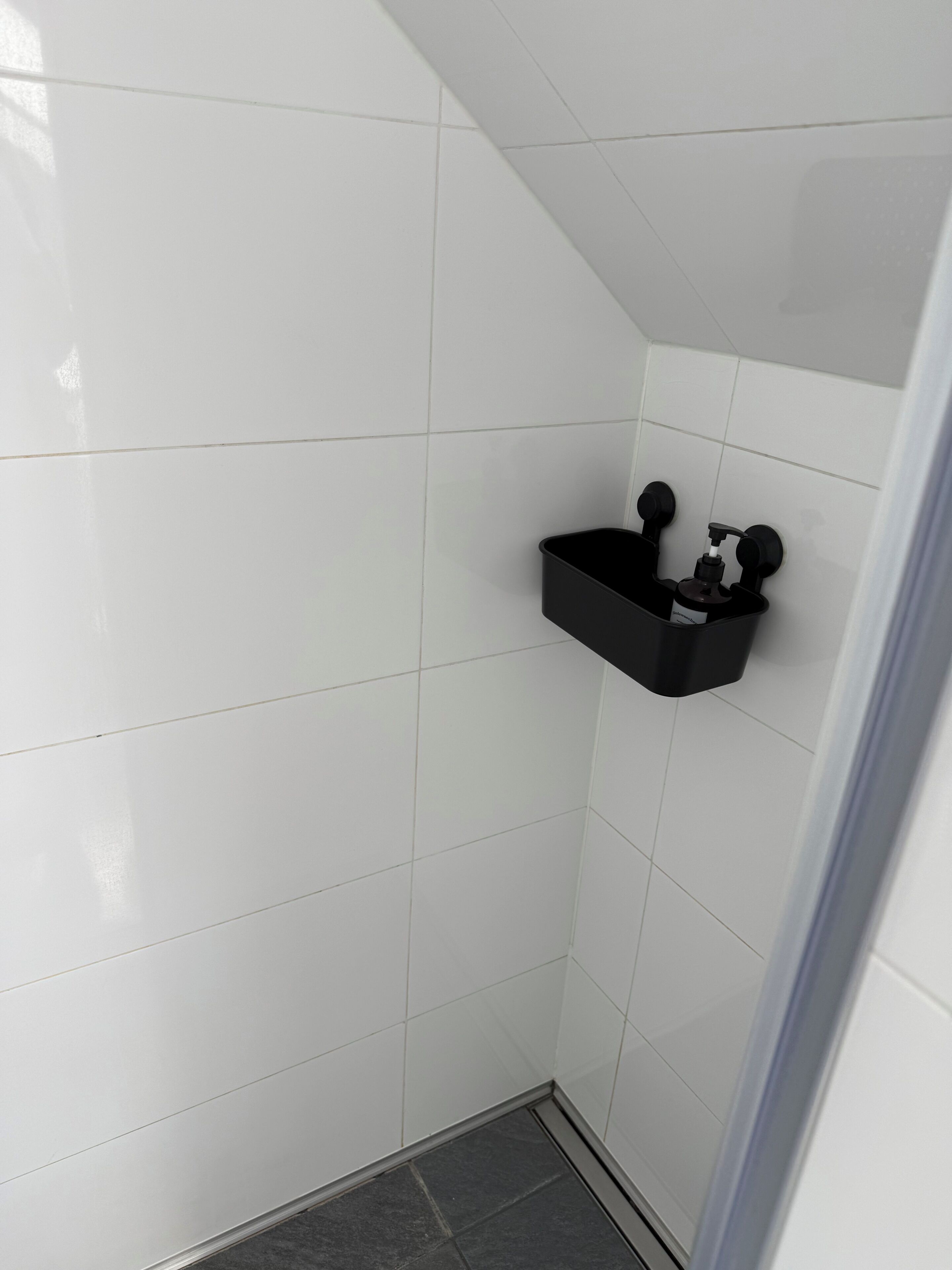 Ein Badezimmer mit weißen Fliesen, einem schwarzen Seifenspender und einem schwarzen Behälter.