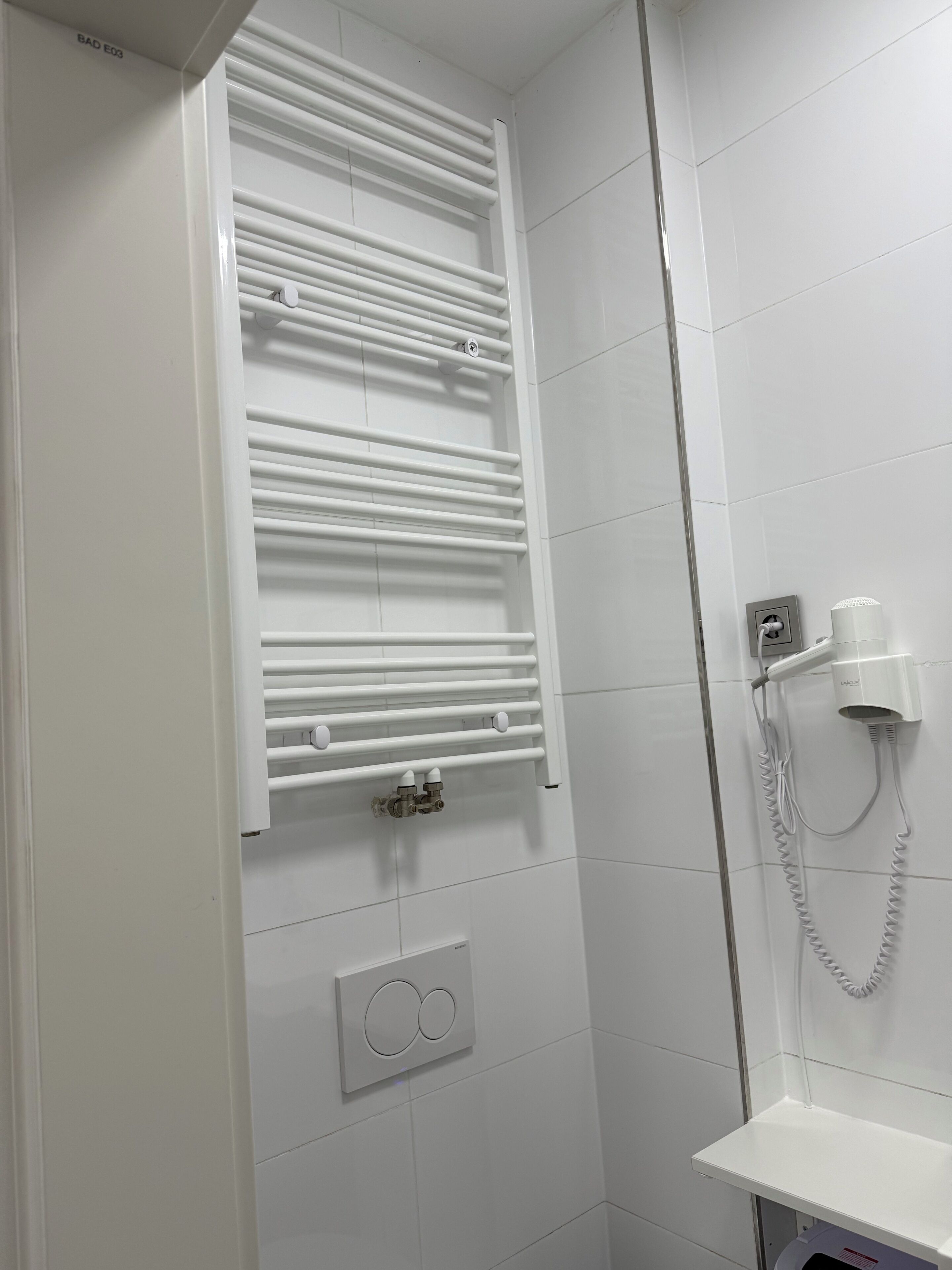 Une salle de bain équipée d’un porte-serviettes blanc, d’un sèche-cheveux et d’un luminaire fixé au mur.