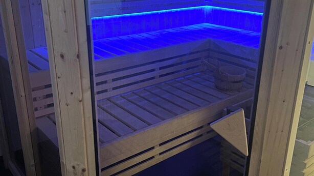 Eine Sauna mit Holzwänden und -bänken, einer sichtbaren Tür und blauem Licht.