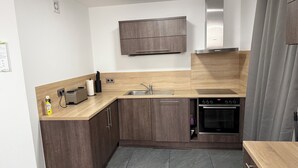 Eine moderne Küche mit Holzausbau, einem Edelstahl-Spülbecken, einem Einbauofen und einer Wand-Mikrowelle.