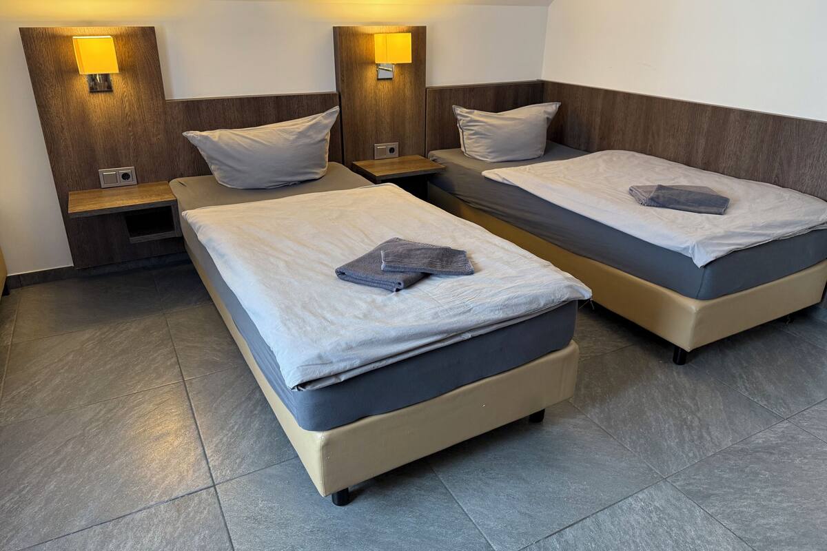 Camera d'albergo con due letti, testiere in legno, lampade sui comodini e un piccolo tavolino di legno.