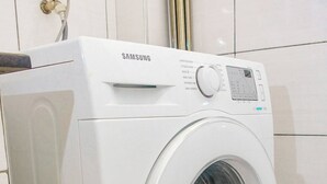 A Samsung front-loading washing machine in a bathroom with white tiled walls and floor. - 'THE TEAL' PREMIUM FURNISHED LUXURY 2-BEDROOM APARTMENT — MOVE-IN READY (Kenya)