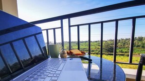A laptop on a glass table with a view of a green landscape through a balcony railing. - 'THE TEAL' PREMIUM FURNISHED LUXURY 2-BEDROOM APARTMENT — MOVE-IN READY (Kenya)