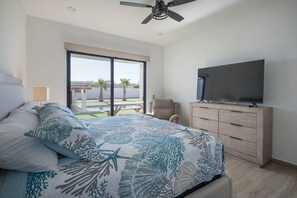 A bedroom with a bed, a TV, a ceiling fan, a window, and a view of the outdoors. - Ocean Breeze Home for 16 guests! (Laguna Shores)