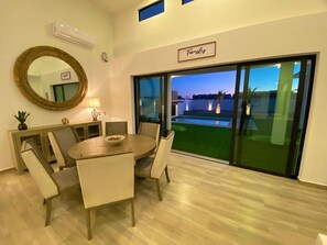 A dining area with a round table and chairs, a large mirror, and a view of a pool through glass doors. - Ocean Breeze Home for 16 guests! (Laguna Shores)