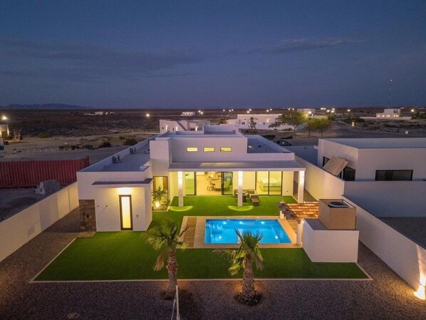 A modern house with a swimming pool, a well-maintained lawn, and a desert landscape in the background. - Ocean Breeze Home for 16 guests! (Laguna Shores)