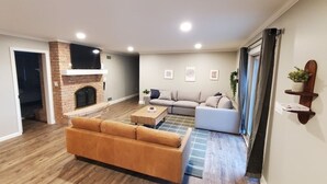 A spacious living room with a fireplace, a sofa, a coffee table, and a TV mounted on the wall. - Amish View Manor - Hot tub w/ Large Outdoor Lot (Lancaster)