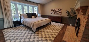 A bedroom with a large bed, a nightstand, a dresser, a fireplace, and a window with curtains. - Amish View Manor - Hot tub w/ Large Outdoor Lot (Lancaster)