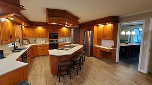 A modern kitchen with wooden cabinets, a central island with stools, stainless steel appliances, and a large window. - Amish View Manor - Hot tub w/ Large Outdoor Lot (Lancaster)
