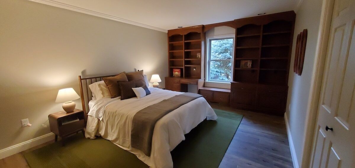 Une chambre à coucher avec un grand lit, des tables de chevet, une fenêtre donnant sur les arbres et des étagères intégrées.