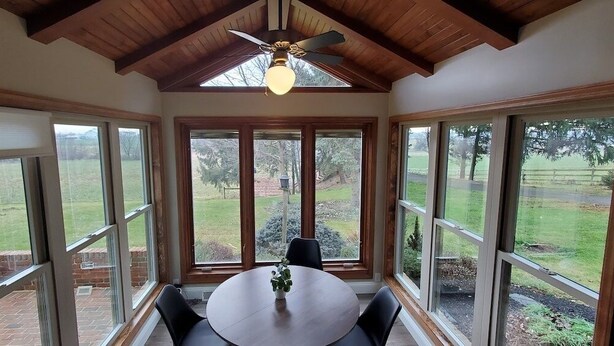 A conservatory with a round table and chairs, large windows, and a ceiling fan. - Amish View Manor - Hot tub w/ Large Outdoor Lot (Lancaster)