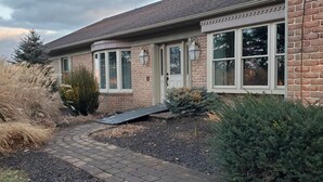 A brick house with a paved driveway, a small ramp, and various shrubs and plants around the entrance. - Amish View Manor - Hot tub w/ Large Outdoor Lot (Lancaster)