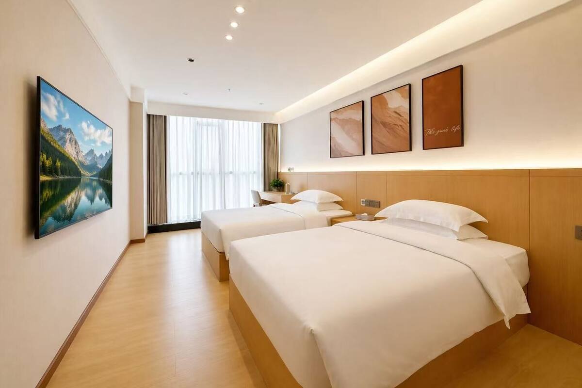 A hotel room with two beds, a large window, and artwork on the walls.