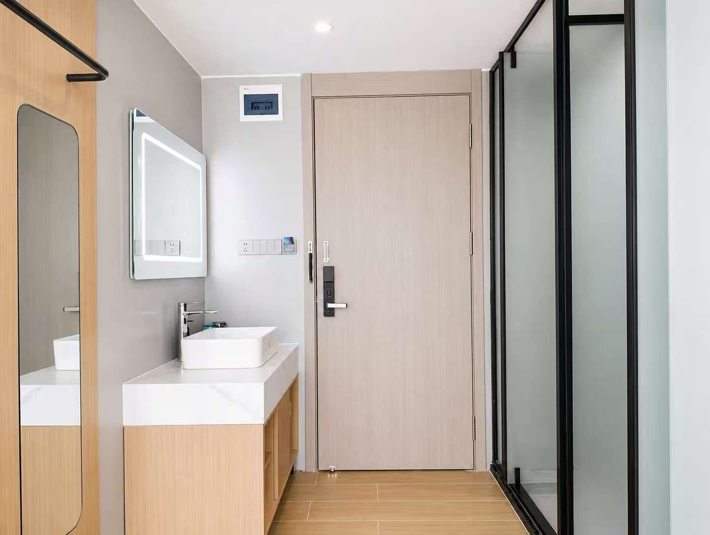 A modern bathroom with a sink, mirror, and a door leading to a glass shower area.