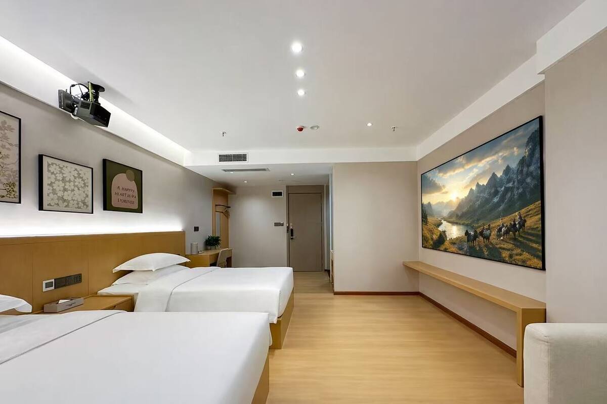 A hotel room with two beds, a desk, a large painting, and a wooden floor.