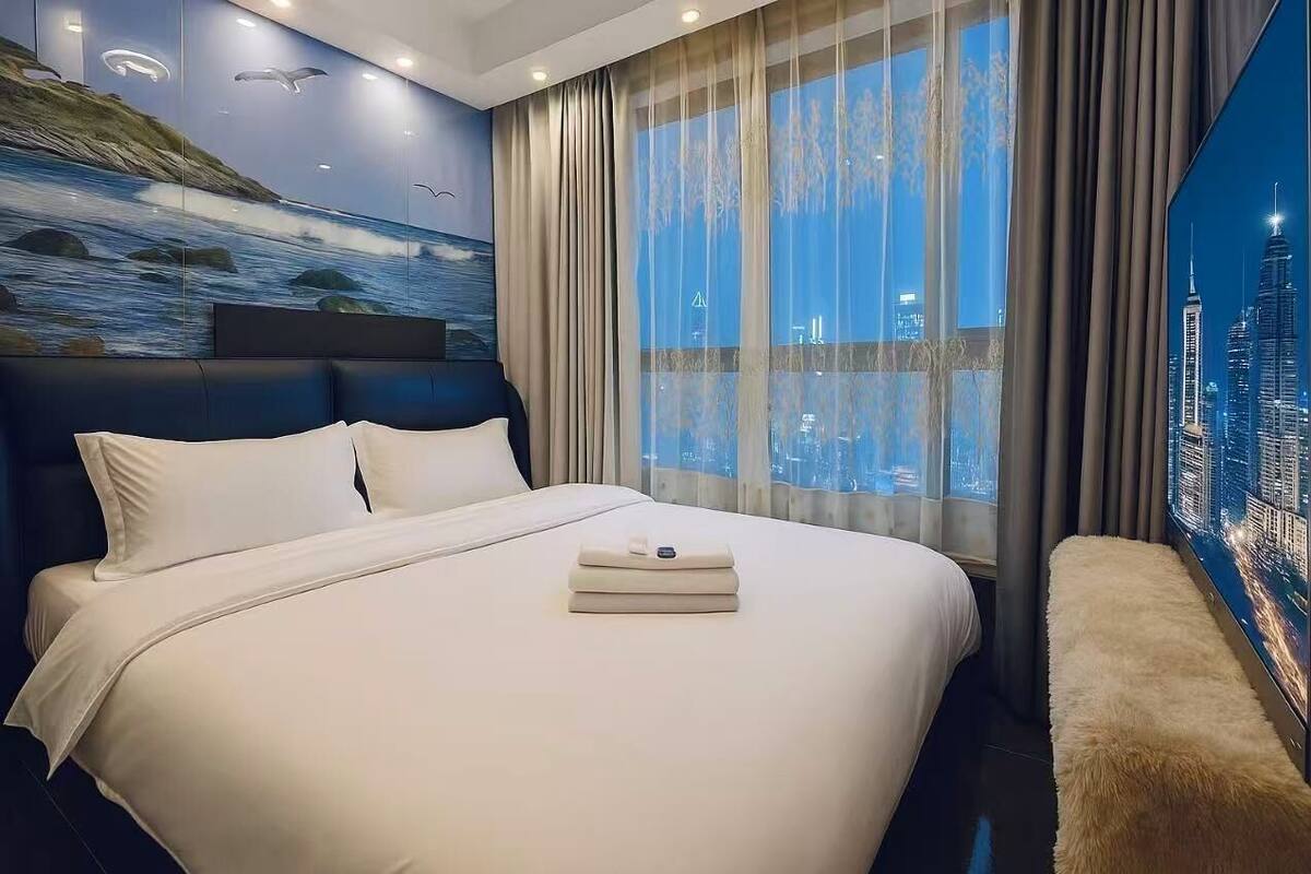 A hotel room with a large bed, a cityscape view, and a mural of a seascape.