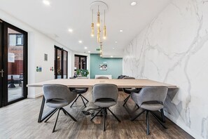Une salle de conférence avec une grande table, quatre chaises grises, un luminaire suspendu et un mur en marbre.