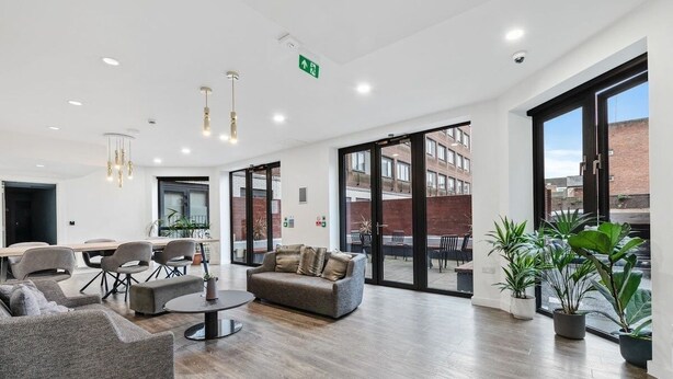 A spacious lobby with a wooden floor, grey sofas, a round coffee table, and potted plants. - Central 2 Bed Flat, Free Parking, Gym, Cinema Room (Bedford)