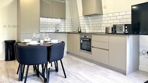 A modern kitchen with a dining area, featuring a black countertop, white tiled backsplash, and a built-in oven. - Central 2 Bed Flat, Free Parking, Gym, Cinema Room (Bedford)