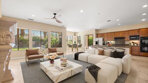 A spacious living room with a large sectional sofa, a marble coffee table, and a dining area with a chandelier. - Desert Luxe Oasis: Private Pool and 4+ BR in Gated South La Quinta! (La Quinta)