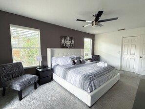 Ein Schlafzimmer mit einem großen Bett, einem Deckenventilator, einem Nachttisch, einem Sessel und einer Tür.