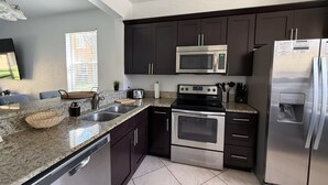 Una cocina moderna con armarios oscuros, electrodomésticos de acero inoxidable, encimeras de granito y lavavajillas.