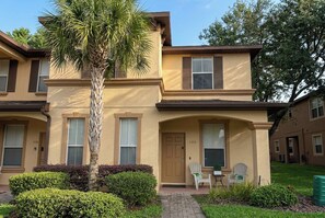 A two-story building with a beige facade, a palm tree, and a small patio with chairs. - Ultimate Townhome-Pool/Lazy River-Waterslide-Hot Tub-Near Disney-No Resort Fees- (Davenport)