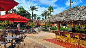 Un patio al aire libre con mesas y sillas, una estructura de techo de paja y palmeras.