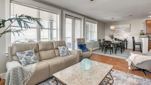 A spacious living room with a beige sofa, a coffee table, and a dining area with a table and chairs. - Beach + Pool Access: Resort Getaway in Galveston! (Galveston)