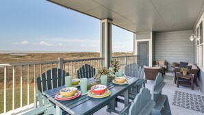 A covered outdoor dining area with a view of the beach, a table set with plates and bowls, and wicker furniture. - Beach + Pool Access: Resort Getaway in Galveston! (Galveston)