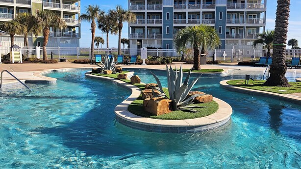 A pool area with multiple water features, palm trees, and a white fence. - Beach + Pool Access: Resort Getaway in Galveston! (Galveston)