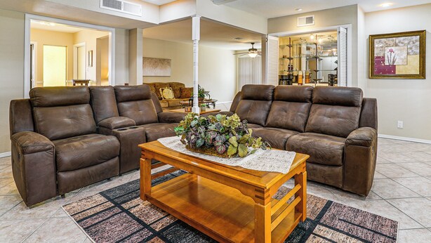 A living room with two brown leather sofas, a wooden coffee table with a floral centerpiece, and a patterned rug. - Patio + Fenced Yard: Group Getaway Near Fort Bliss (El Paso)