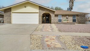 A single-story house with a garage, a stone pathway leading to the entrance, and a palm tree in the background. - Patio + Fenced Yard: Group Getaway Near Fort Bliss (El Paso)