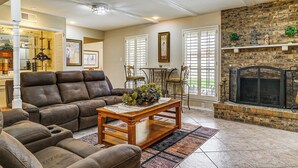 A living room with a fireplace, a sofa, a coffee table, and a dining area with chairs. - Patio + Fenced Yard: Group Getaway Near Fort Bliss (El Paso)