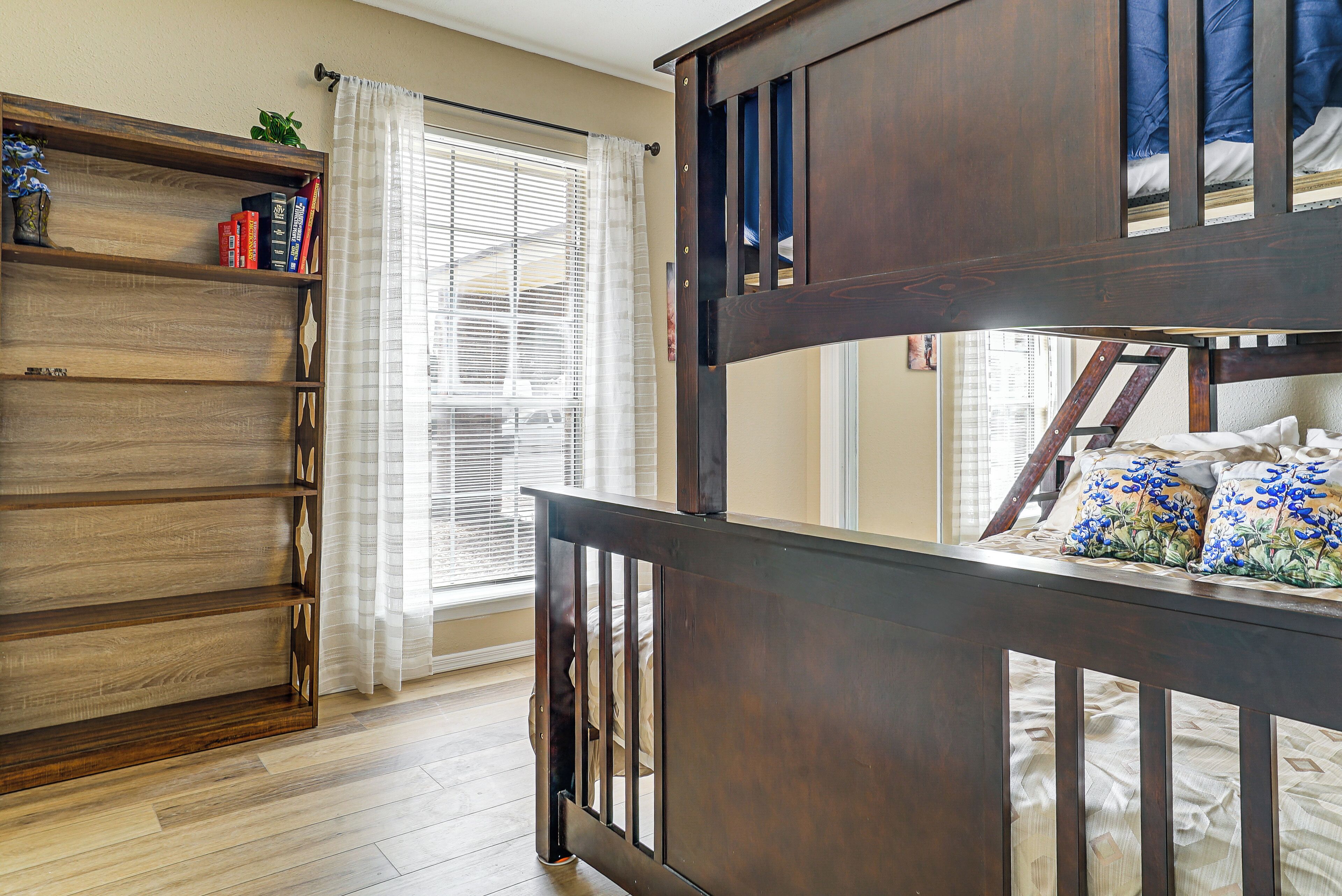 A room with a bunk bed, a wooden bookshelf, and a window with curtains.