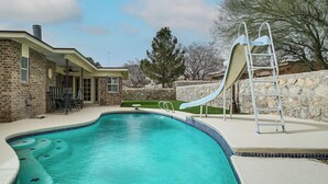 A swimming pool with a slide, a ladder, and a stone wall. - Patio + Fenced Yard: Group Getaway Near Fort Bliss (El Paso)