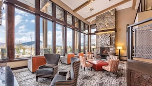 A spacious lounge with large windows, comfortable seating, and a stone fireplace. - Spacious 3 bedroom in Magical Park city Utah (Park City)