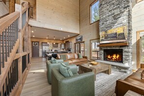 A spacious living area with a stone fireplace, wooden floors, and a high ceiling. - Easy Stony- New- Hot Tub- Game Room- LUX (Sevierville)