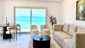A modern living room with a view of the sea, a round coffee table, a beige sofa, and a dining area with chairs. - Double Accommodation on the Waterfront in La Marsa (La Marsa)