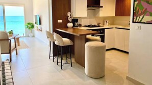 A modern kitchen with a bar area, white cabinets, and a view of the sea. - Double Accommodation on the Waterfront in La Marsa (La Marsa)