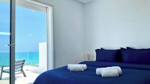 A hotel room with a large bed, two pillows, and two towels. There is a chair and a lamp on a small table. The room has a large window with a view of the ocean. - Double Accommodation on the Waterfront in La Marsa (La Marsa)